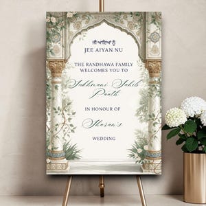 Könnte beinhalten: Hochzeit Willkommensschild mit aufwendigem architektonischem Design, floralen Akzenten und Text in Englisch und einer anderen Sprache. Das Schild wird auf einer goldenen Staffelei mit einer goldenen Vase mit weißen Blumen an der Seite angezeigt.