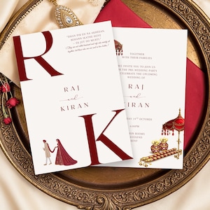 Może przedstawiać: Karty zaproszeń ślubnych z bordowymi akcentami. Karty zawierają imiona "Raj i Kiran" w eleganckim skrypcie, z dekoracyjnymi ilustracjami i tekstem. Karty są umieszczone na dekoracyjnym złotym talerzu.