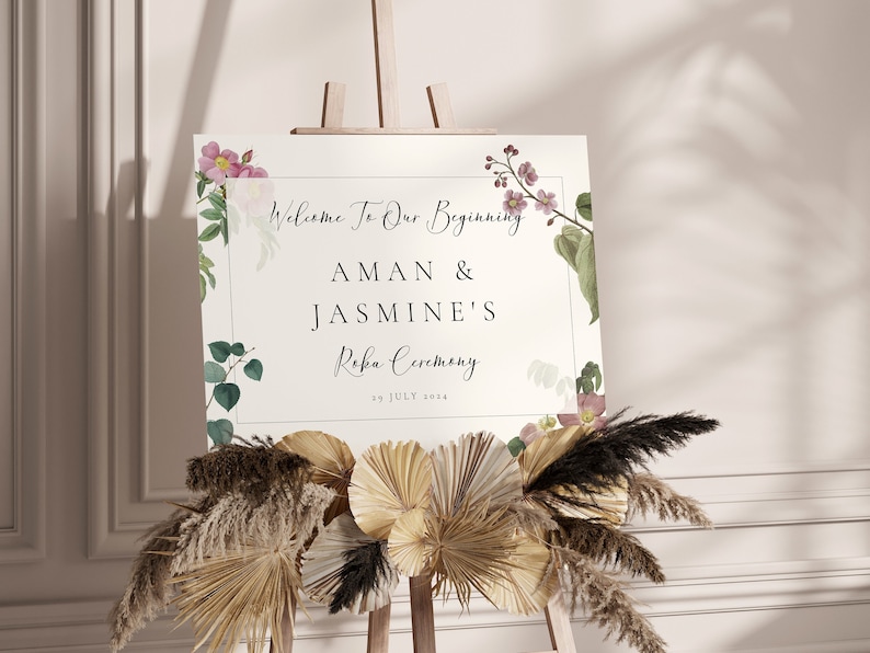 May include: A wedding welcome sign on an easel, featuring floral accents and the text "Welcome To Our Beginning" with names and date. The sign is decorated with dried flowers and greenery.