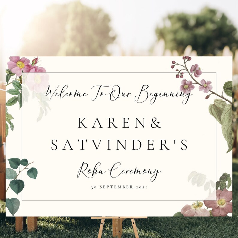 May include: A cream-colored sign with floral accents and the text "Welcome To Our Beginning" above the names "KAREN & SATVINDER'S Roka Ceremony" and the date "30 SEPTEMBER 2021". The sign is displayed on a wooden easel.