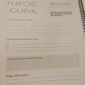 K&ouml;nnte beinhalten: Ein wei&szlig;es Journal mit den Worten "Purpose Journal" oben. Das Journal hat Abschnitte f&uuml;r t&auml;gliche Affirmationen, Dinge, die dich heute zum L&auml;cheln gebracht haben, und etwas, das dich heute inspiriert hat. Es hat auch einen Abschnitt, um drei Dinge aufzuschreiben, auf die du hinarbeitest.