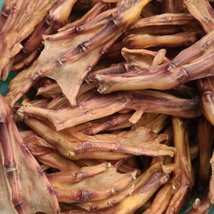 May include: A bowl filled with dried duck feet, a popular dog treat. The feet are a light brown color with some darker brown areas. They are arranged in a random pattern.
