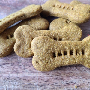 May include: A close-up of several dog biscuits in the shape of bones. The biscuits are a light brown color and have the word "Imperie" imprinted on them.