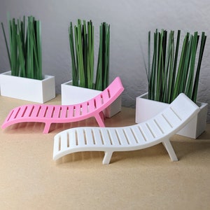May include: A miniature pink and white lounge chair with a slatted design. The chairs are placed in front of white rectangular planters filled with green grass. The background is a neutral gray.