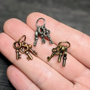 May include: Three sets of antique-style keys in bronze, silver, and gold tones. Each set features multiple keys attached to a small ring. The keys have intricate designs and varying sizes, suggesting a vintage or steampunk aesthetic.
