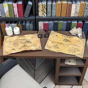 May include: Miniature brown desk with two maps, Isbaela and Erythimor, and small black glasses. The desk has a chair and is in front of a bookshelf filled with miniature books. The maps are tan with black text and illustrations.