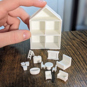 May include: A white miniature dollhouse with four rooms and a pitched roof, accompanied by small white furniture pieces. The furniture includes a ladder, stove, table, chairs, sofa, and a fireplace. The dollhouse and furniture are made of a solid white material.