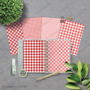 May include: Four sheets of red and pink gingham patterned paper. The paper is arranged in a square shape with a binder in the center. The binder is open and shows the same gingham pattern on the inside. A gold pen and a roll of washi tape are on the table.