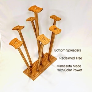 May include: A wooden display stand featuring multiple vertical supports with flat, rounded tops. The stand is made from reclaimed wood and has the text "Bottom Spreaders", "Reclaimed Tree", and "Minnesota Made with Solar Power".