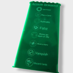 Pu&ograve; includere: Foglio di acrilico verde con simboli di azione incisi per un gioco da tavolo. I simboli includono: Guadagnare potere, Giocare una carta, Attiva, Destino, Spostare un oggetto o un alleato, Spostare un eroe, Vincere e Scartare carte.