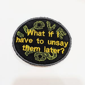 May include: A black and yellow embroidered patch with the text "What if I have to unsay them later?" surrounded by a green and black pattern.