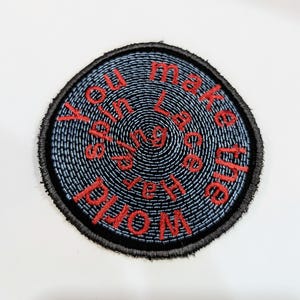 May include: A round, black and blue embroidered patch with the text "You make the world spin" in red.