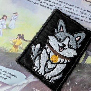 May include: A black and white embroidered patch of a cartoon dog holding a gold coin. The dog is smiling and has a brown collar.