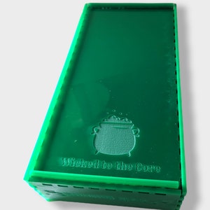 Pu&ograve; includere: Una scatola verde con un calderone e il testo "Wicked to the Core" sul davanti.