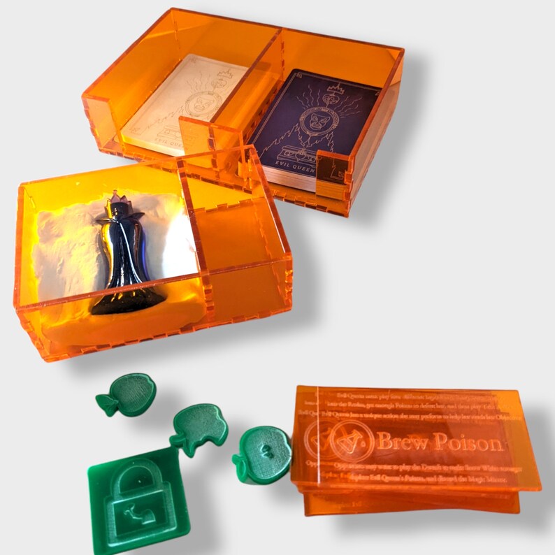 Pu&ograve; includere: Scatole di immagazzinaggio in plastica arancione con scomparti per pezzi di gioco e carte. Le scatole contengono una statuetta in miniatura, una carta con il testo "Evil Queen" e una carta con il testo "Brew Poison".