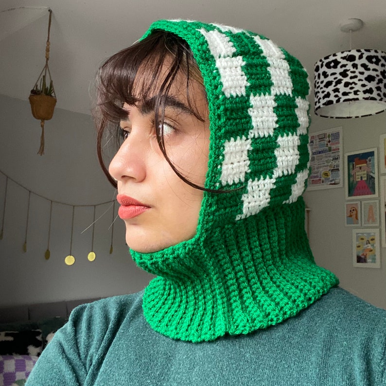Pode incluir: Uma balaclava de croch&ecirc; verde e branca com um padr&atilde;o xadrez. A balaclava est&aacute; sendo usada por uma pessoa com cabelo escuro.