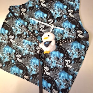 May include: A black and blue Harry Potter themed apron with white outlines of Hogwarts castle and the words "Harry Potter" repeated throughout. The apron has a white ribbon and a black and white polka dot ribbon attached.