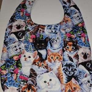 May include: A blue fabric bib with a pattern of many colorful cats and flowers. The bib has a rounded neck opening.