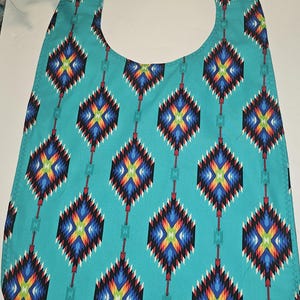 May include: A turquoise bib with a geometric pattern in shades of red, blue, yellow, and black. The pattern is reminiscent of Native American designs.