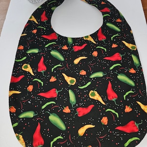 May include: Black bib with a red, yellow, and green chili pepper pattern. The bib has a rounded neck opening.