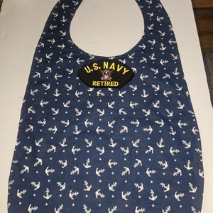 May include: A blue fabric bib with a white anchor pattern. The bib has a U.S. Navy patch with the words "U.S. NAVY RETIRED" on it.