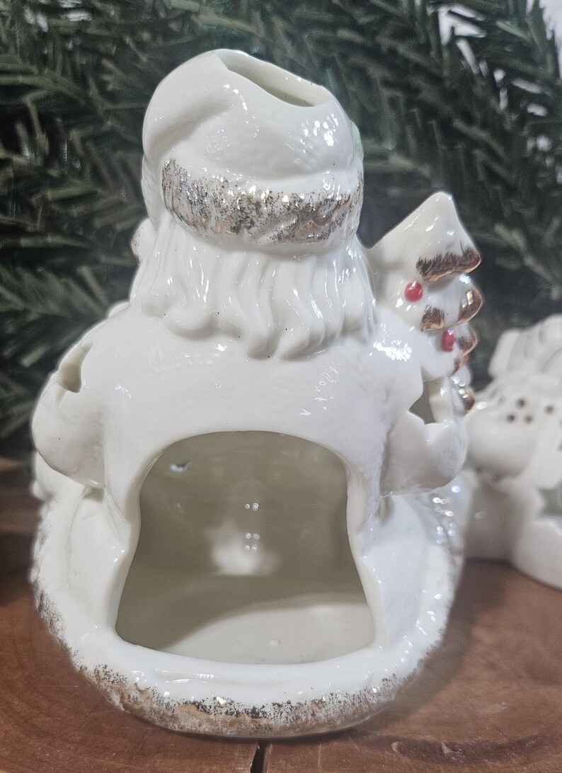 Puede incluir: Una figura de Pap&aacute; Noel de cer&aacute;mica blanca con la parte trasera hueca, con detalles de purpurina dorada en el gorro y la base, y un peque&ntilde;o &aacute;rbol con puntos rojos en la mano. La superficie brillante refleja la luz, resaltando la barba y el gorro.