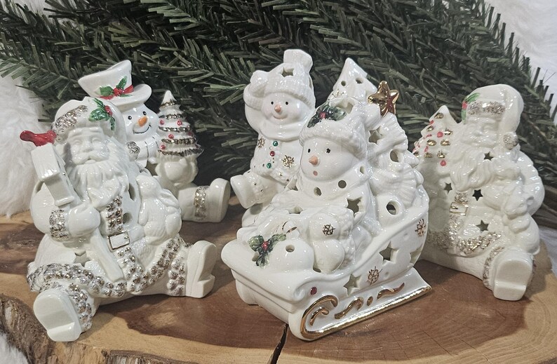 Puede incluir: Una colecci&oacute;n de figuras navide&ntilde;as de cer&aacute;mica blanca que incluye a Santa Claus, mu&ntilde;ecos de nieve y un trineo. Cada pieza presenta detalles en dorado y plateado, hojas de acebo y aberturas en forma de estrella para dejar pasar la luz.