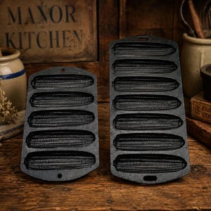 May include: Two black cast iron corn stick pans with textured, ear-of-corn shaped molds. The left pan features five individual molds, while the right pan features seven individual molds. Both pans have a small hole at the top for hanging.