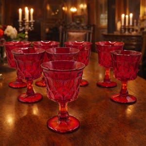 May include: A collection of ruby red wine glasses with a diamond pattern. The glasses are arranged on a wooden table, with a warm, inviting ambiance. The stemware is ideal for serving wine or other beverages.