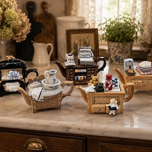 May include: A collection of four ceramic teapots shaped like miniature furniture pieces, including a black stove, a brown desk with a typewriter, a light brown vanity with a washbasin, and a light brown table with a toy soldier and teddy bear.