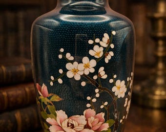 May include: A dark teal vase with a gold rim and silver base, adorned with a floral design. The artwork features white blossoms and pink peonies on a dark background, creating a striking contrast. The vase is a decorative item.