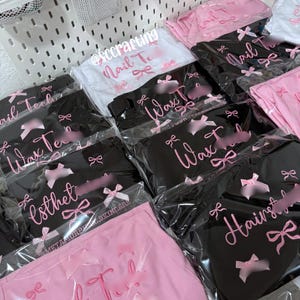 May include: An assortment of packaged beauty products, including black and pink items. The products are labeled with pink text, featuring words like "Nail Tech," "Wax Tech," and "Esthet." The packaging includes pink bows.