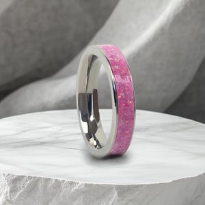May include: A silver ring with a pink glitter band. The ring is on a white marble surface.