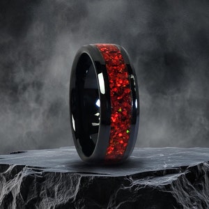 May include: A black ceramic ring with a red glitter inlay. The ring is sitting on a gray rock.