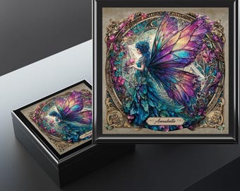 May include: A black box with a hinged lid, featuring a colorful illustration of a fairy with butterfly wings. The fairy is surrounded by flowers and ornate gold detailing. The name "Annabelle" is written on the bottom of the image.