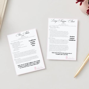 May include: Two white papers with text, titled "Love & Kindness Ahead" and "Save Shalom". A gold pen, a pink notebook, and a small wooden bowl with pink paperclips are also on the white surface. A small vase with red flowers is in the background.