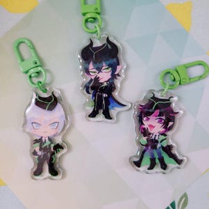 Può includere: Tre portachiavi in acrilico con personaggi dei cartoni animati, chiusure verdi e dettagli verdi. I personaggi hanno diversi colori di capelli e abiti. I portachiavi sono su uno sfondo a motivi.