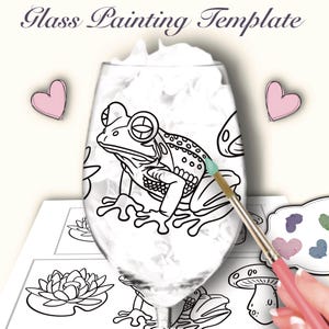 Puede incluir: Una copa de vino transparente con un diseño de contorno de rana, parte de una plantilla de pintura sobre vidrio. La imagen incluye un pincel aplicando pintura, una paleta y el texto "Glass Painting Template". Dos corazones rosas están a los lados.