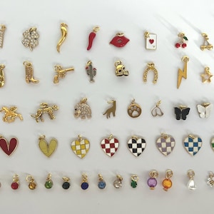 May include: A collection of 50 gold-tone charms with various designs, including hearts, stars, animals, and symbols. The charms are arranged in rows on a white background.