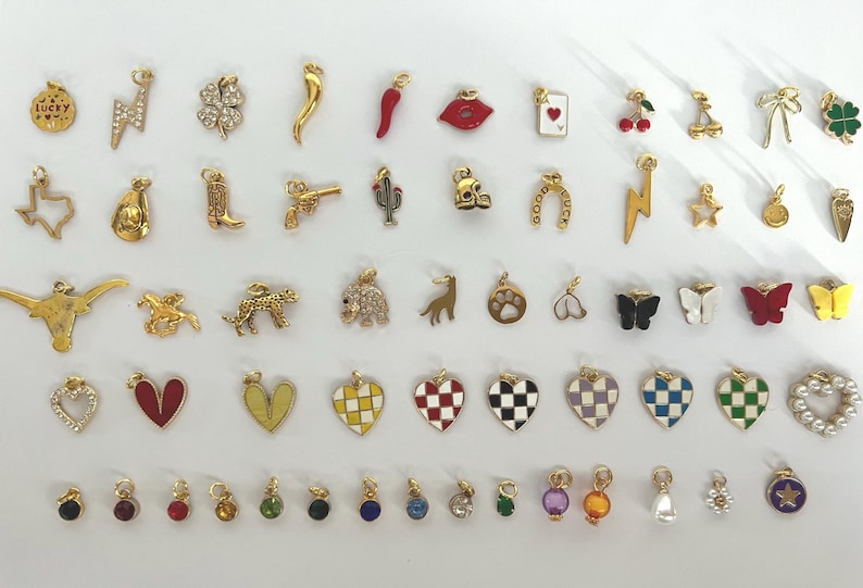 May include: A collection of 50 gold-tone charms with various designs, including hearts, stars, animals, and symbols. The charms are arranged in rows on a white background.
