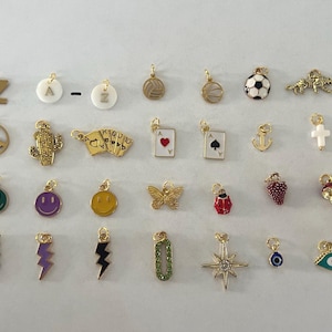 May include: A collection of 30 gold charms with various designs, including letters, animals, sports, and symbols. The charms are all about 1 inch in size and have a loop at the top for attaching to a necklace or bracelet.