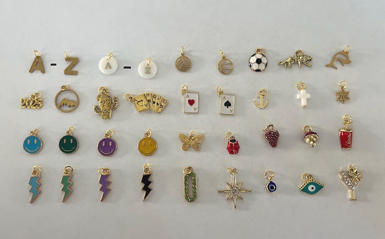 May include: A collection of 30 gold charms with various designs, including letters, animals, sports, and symbols. The charms are all about 1 inch in size and have a loop at the top for attaching to a necklace or bracelet.