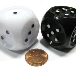 May include: Two spherical dice, one white and one black, each with black or white dots representing numbers. A penny is placed between the dice for size comparison. The dice are a gaming accessory.