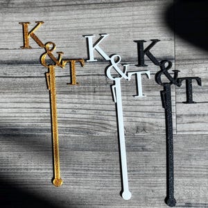 May include: Three cake toppers with the letters K & T, one gold, one white, and one black.