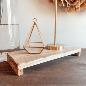 May include: A wooden tray with a gold geometric glass terrarium and a gold metal lamp on top. The tray is sitting on a dark wood surface.
