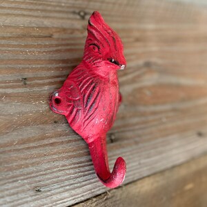 Peut inclure: Crochet rouge en forme de cardinal. Le crochet est en métal et a la forme d'un cardinal avec un bec courbé et un crochet en bas. Le crochet est monté sur une surface en bois.