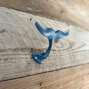 May include: A blue metal whale tail hook mounted on a light brown wooden wall.