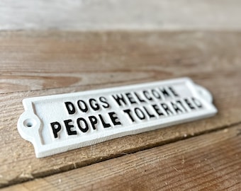 May include: White metal sign with black text that reads "Dogs Welcome People Tolerated".