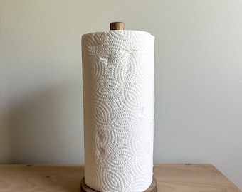 May include: A wooden paper towel holder with a white paper towel roll. The holder has a natural wood finish and a round base.