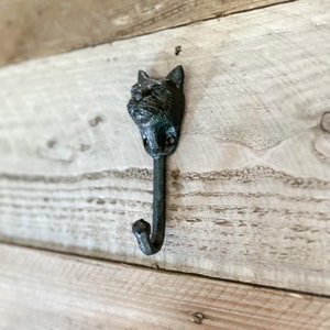 May include: A black cast iron cat head hook mounted on a light wood wall.